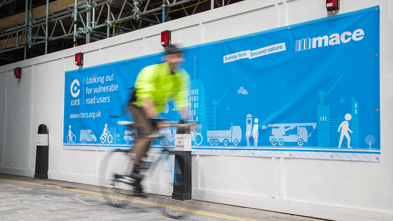 Cyclists Passing by a Mace Banner - Mace Group